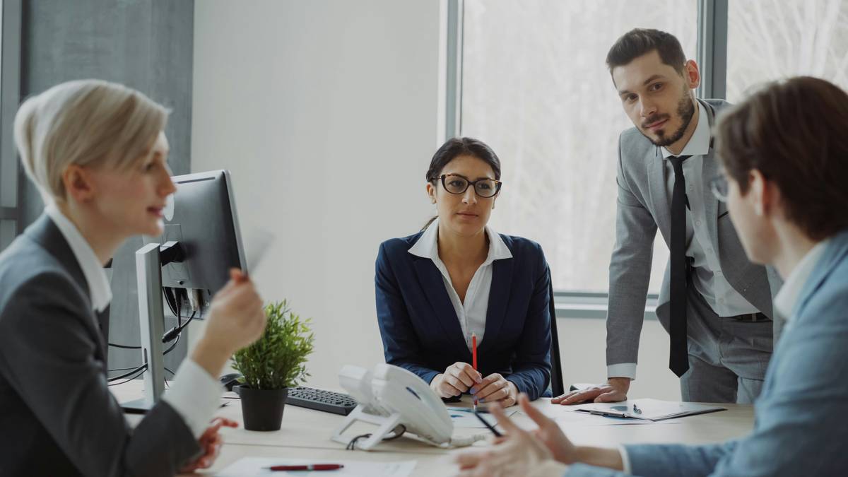 Business networking events today: diverse professionals collaborating in a modern hybrid workspace with laptops, whiteboards, and casual conversation